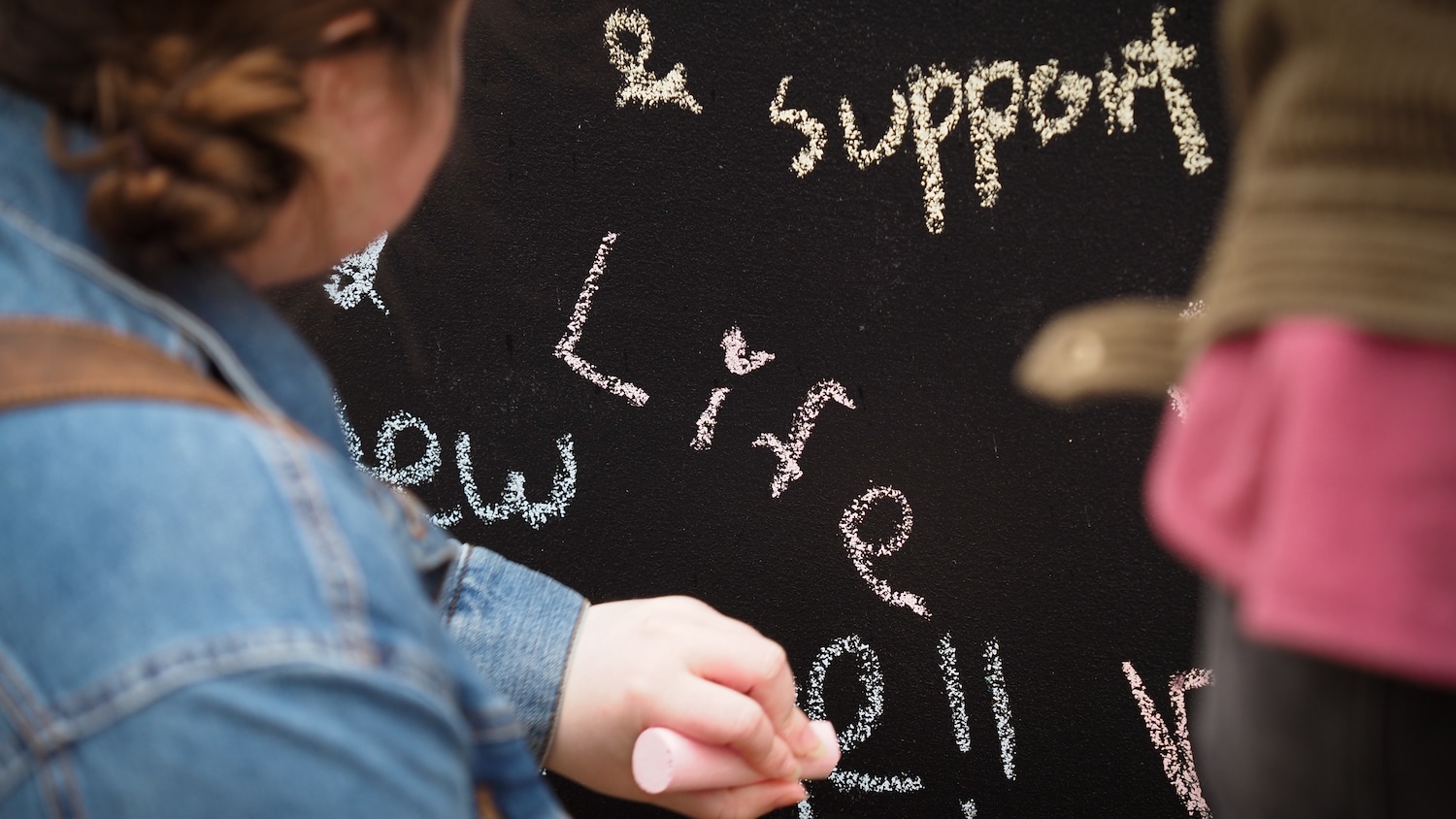 Students write "life" on a chalk wall during an annual Day of Giving event.