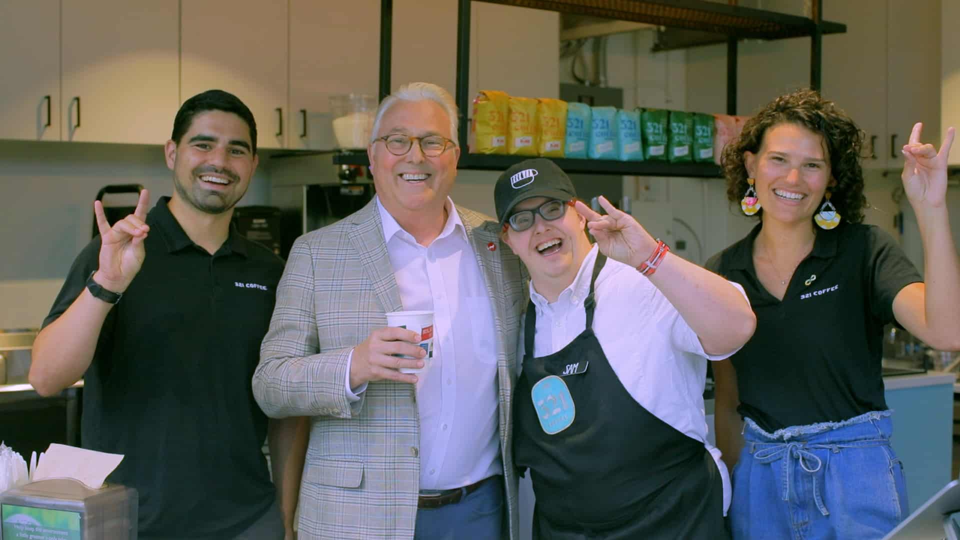 Chancellor Woodson poses for a photo in the downtown Raleigh 321 Coffee shop with barista Sam and co-founder Laurie Henes to his left and co-founder Michael Evans to his right.