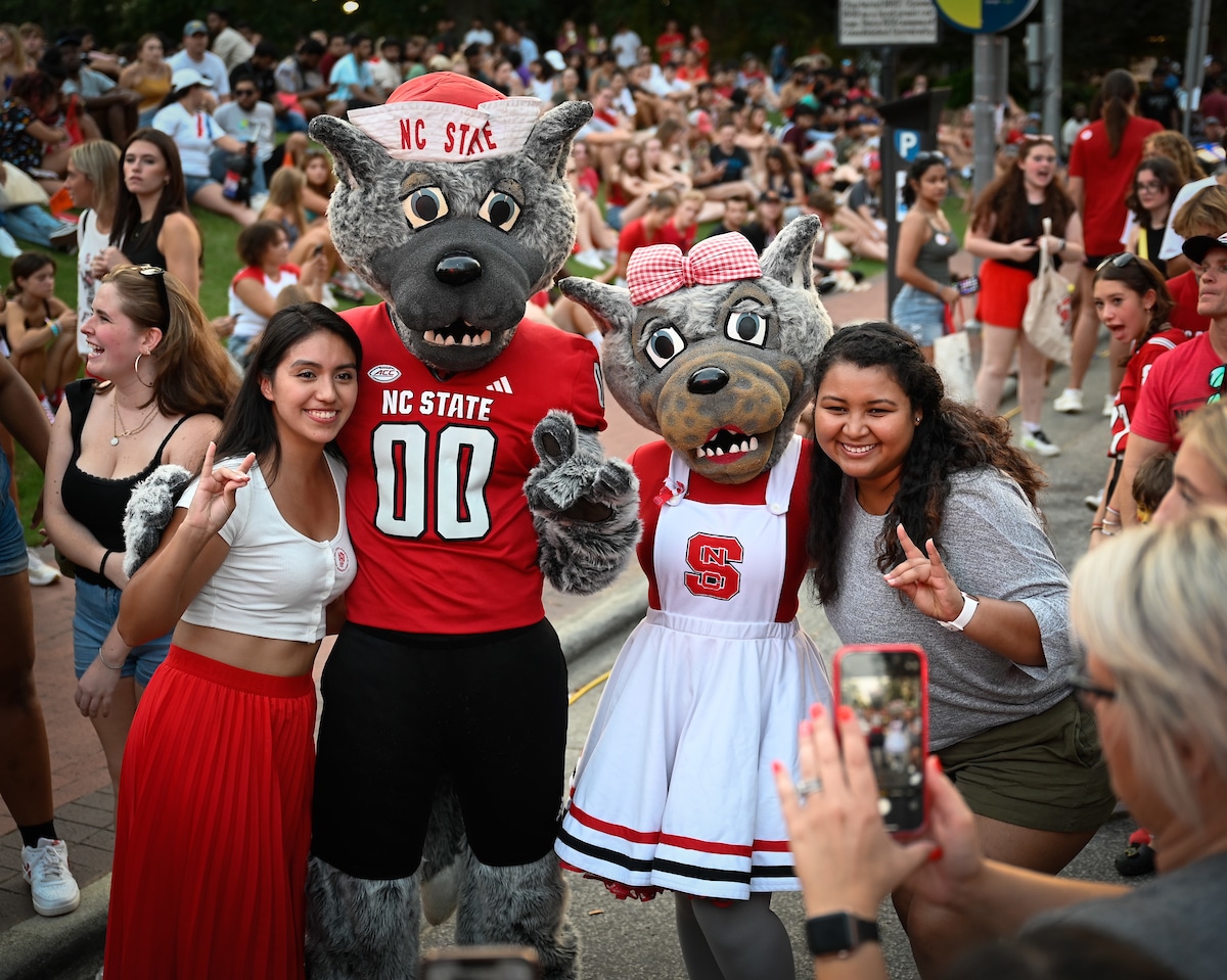 The NC State mascots, Mr. Wuf and Mrs. Wuf, pose with two students on a crowded Hillsborough Street during Packapalooza 2023.