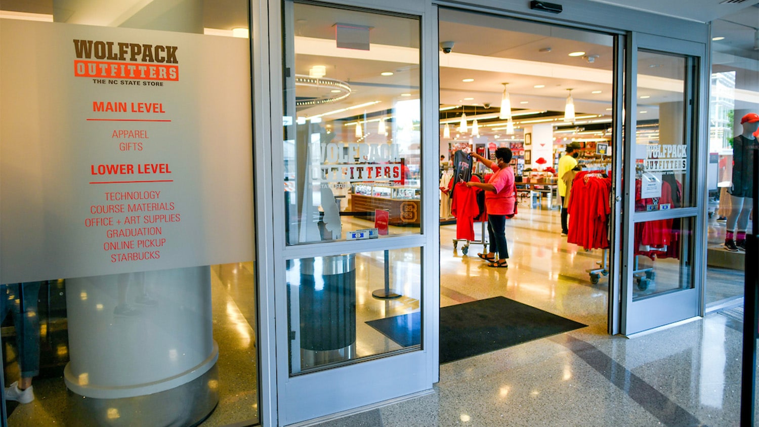 The entrance to NC State's Wolfpack Outfitters campus store. Inside, a customer wearing examines a T-shirt that they took off the rack.