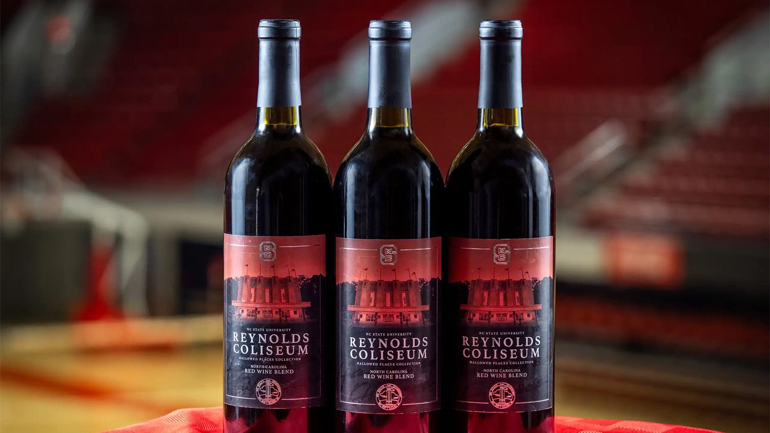 Three bottles of red wine sitting on a table in the middle of the gymnasium in Reynolds Coliseum.