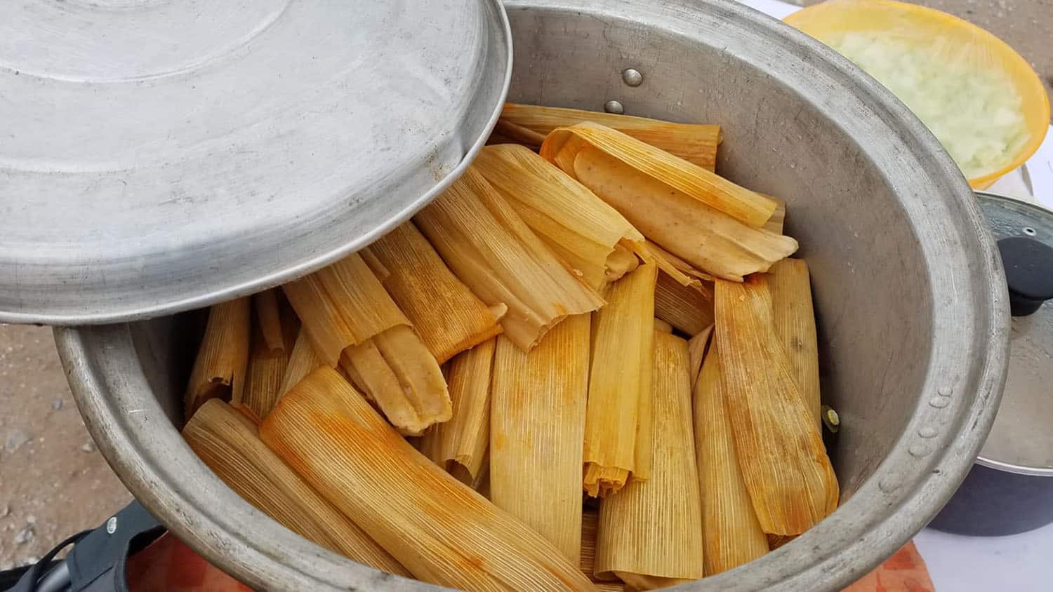 more than a dozen tamales, wrapped in corn husks, sit inside a large metal pot