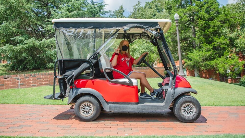 NC State student drives the Wolfpack Pick Up golf cart through the Court of North Carolina.