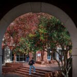 A student is seen through an archway, walking up stairs between buildings on campus.