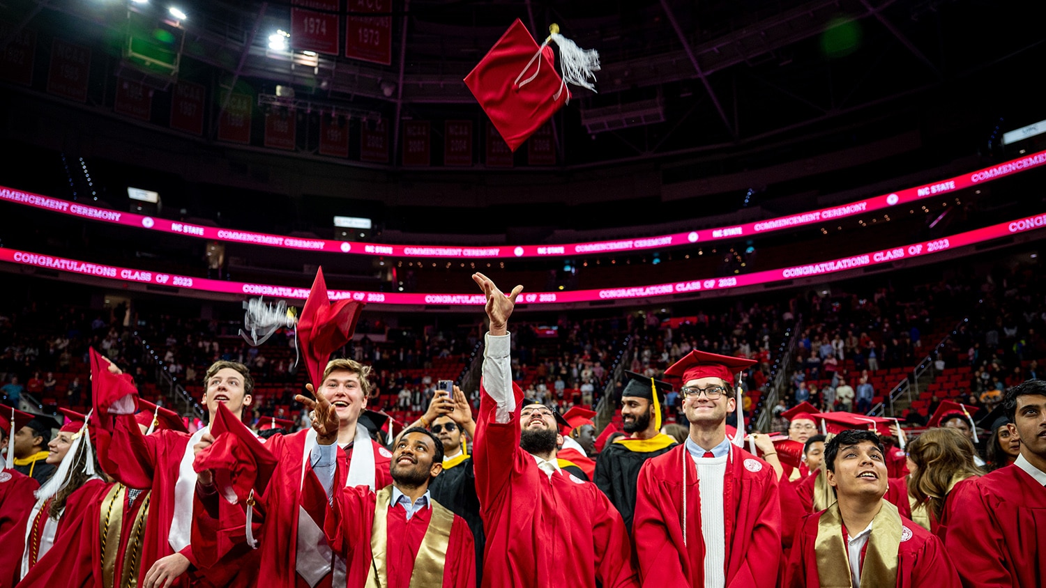 Students smile and toss their graduation caps in the air during commencement.