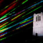 Colorful laser lights surround the Memorial Belltower at night.