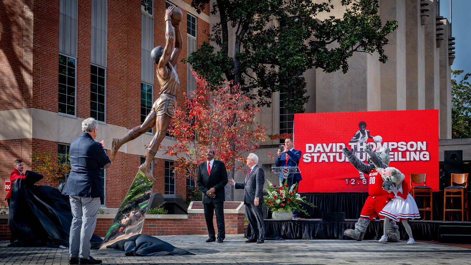 David Thompson and other attendees watch as a black sheet is removed to reveal a new statue in his likeness next to Reynolds Coliseum.