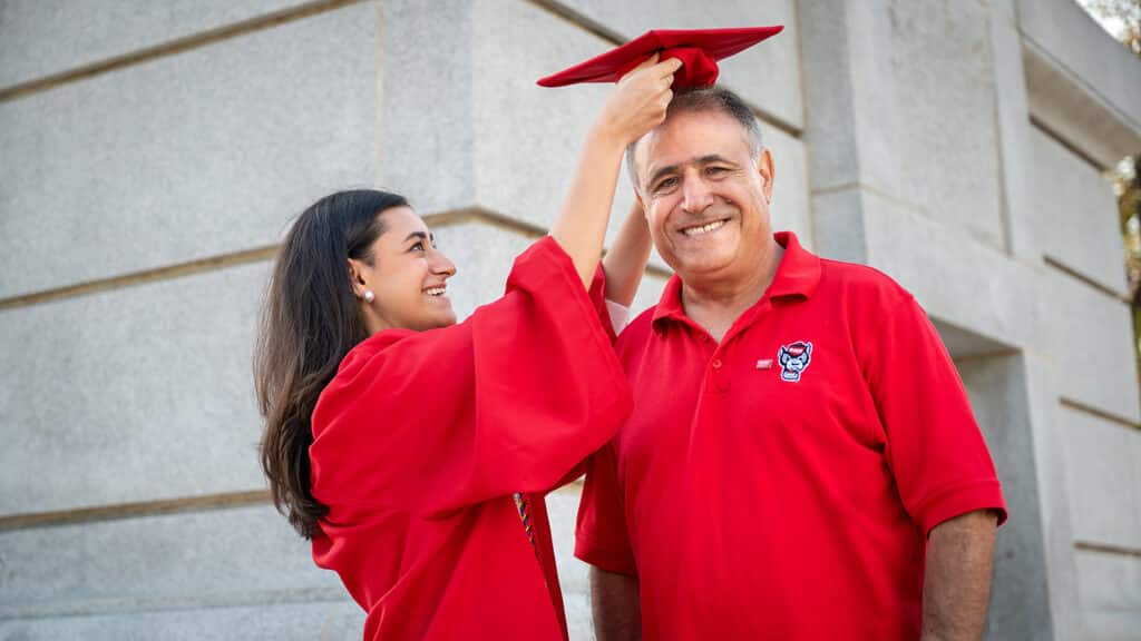 Kemmia Ghodrat places her red mortar board  on her father's head. The two are standing in front of the Memorial Belltower. 
