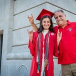 Kemmia and Hushang Ghodrat stand in front of the Memorial Belltower. Kemmia wears her red graduation robe and mortar board.