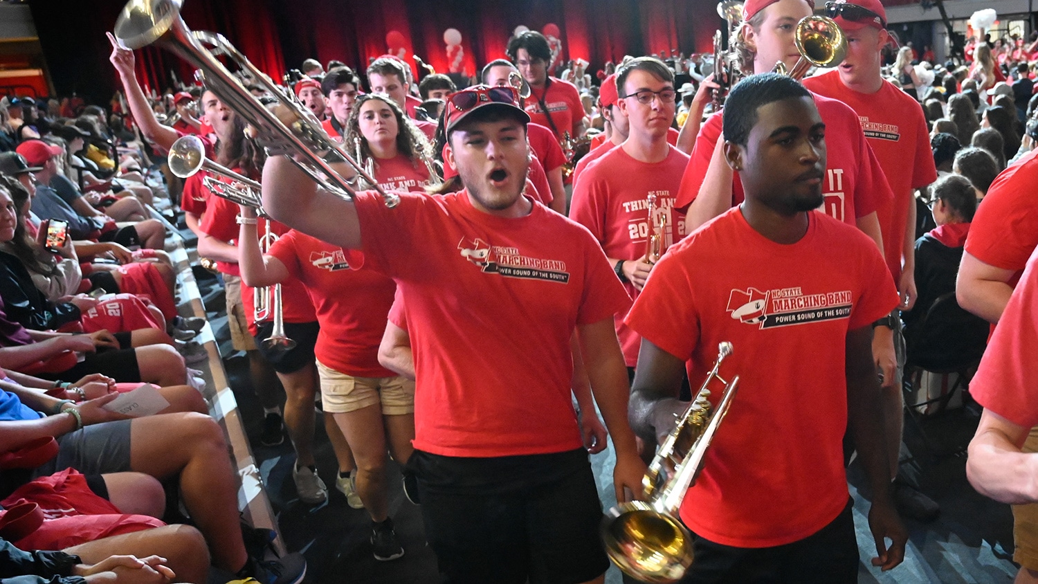 Members of the marching band march into Reynolds Coliseum wearing branded Power Sound of the South T-shirts.