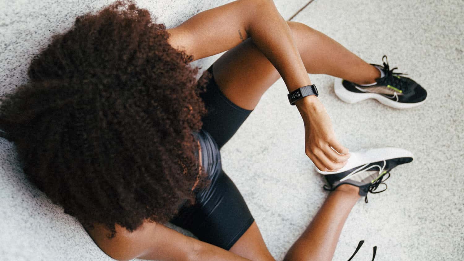photo taken from above shows a Black woman in exercise clothes looking at a health monitor on her wrist