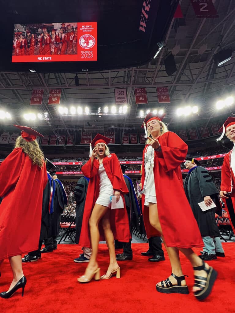 Students in red robes wave at the camera as they prepare for commencement.