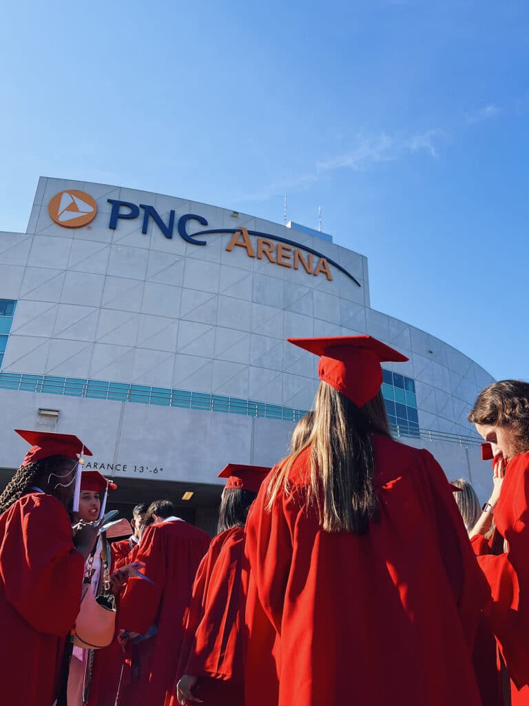 Students in red robes gather to enter PNC Arena before spring commencement.