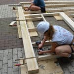 Students use electric drills to drill holes in pieces of wood as they construct the framework for a structure.