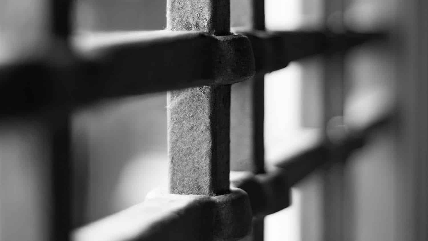 black and white photo shows the bars of a prison cell