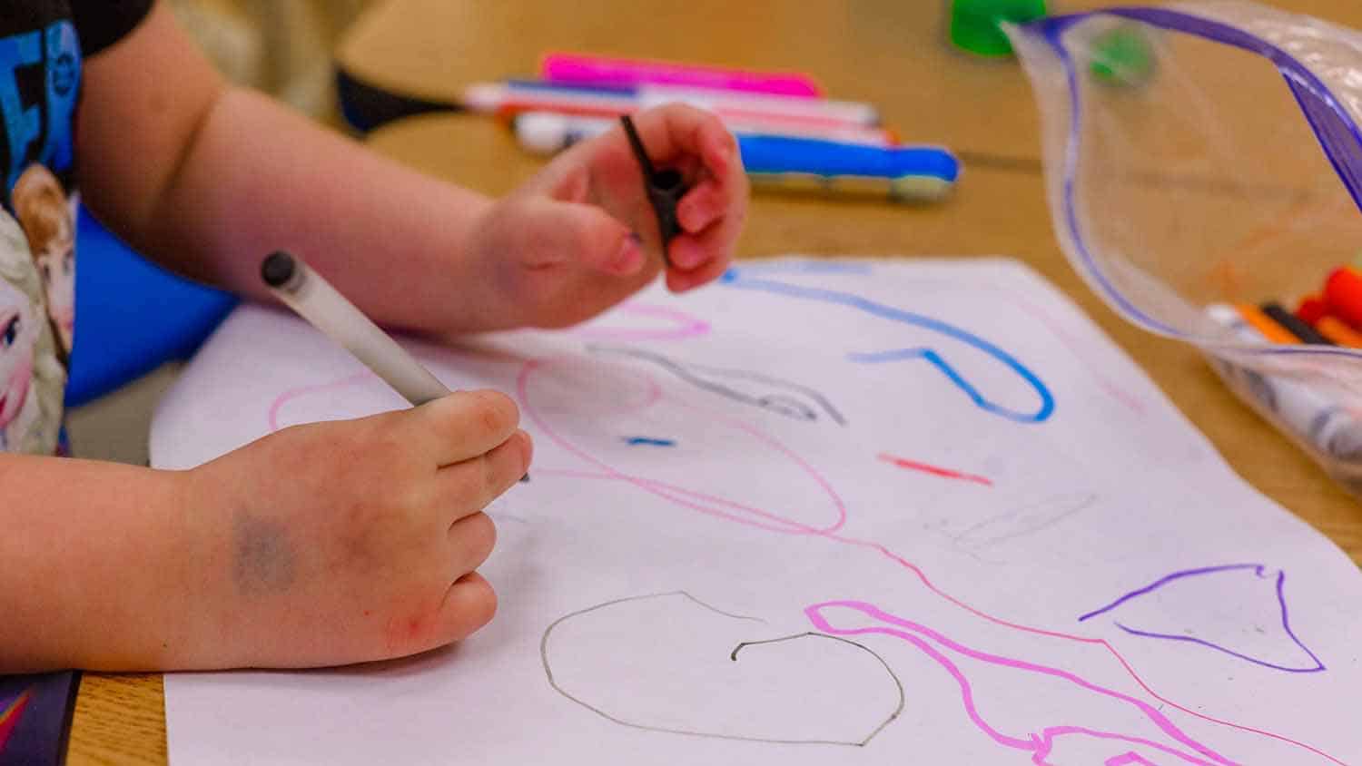 photo shows young child's hands coloring with magic markers