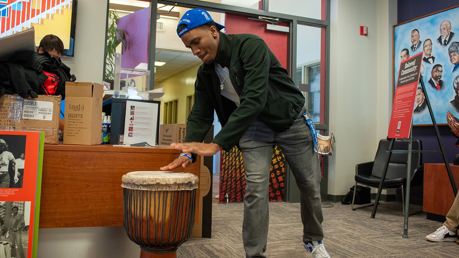 A student drums on a djembe sitting on the floor just inside the door of the African American Cultural Center in Witherspoon Student Center.