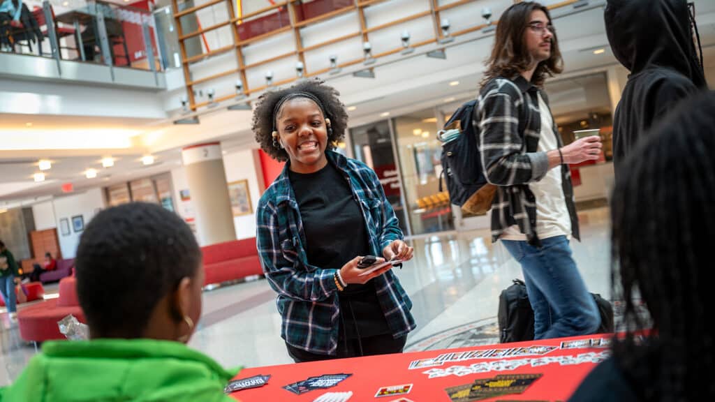 A student picks up handouts from a table inside Talley Student Union during the Black History Month kickoff event while other students walk by.