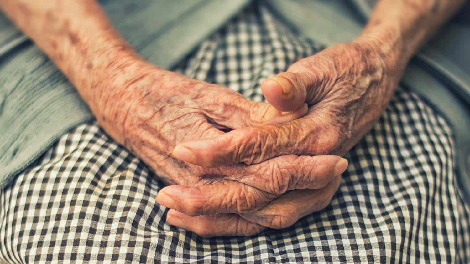an old woman's hands are folded in her lap