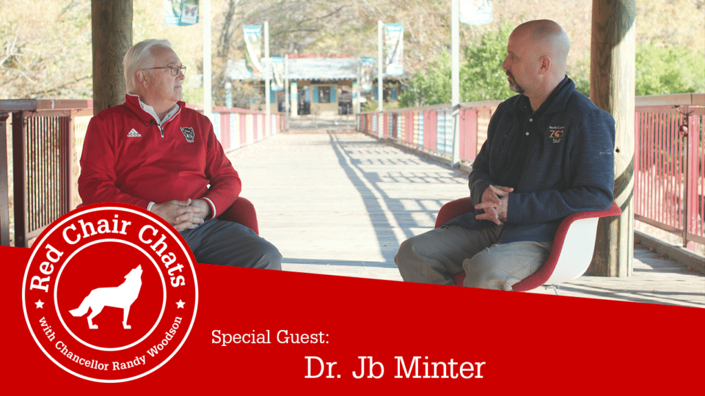 Chancellor Woodson and Dr. Jb Minter sit at the Africa entrance of the North Carolina Zoo. The image also contains the Red Chair Chats graphic, which says "Red Chair Chats with Chancellor Woodson. Special guest: Dr. Jb Minter."