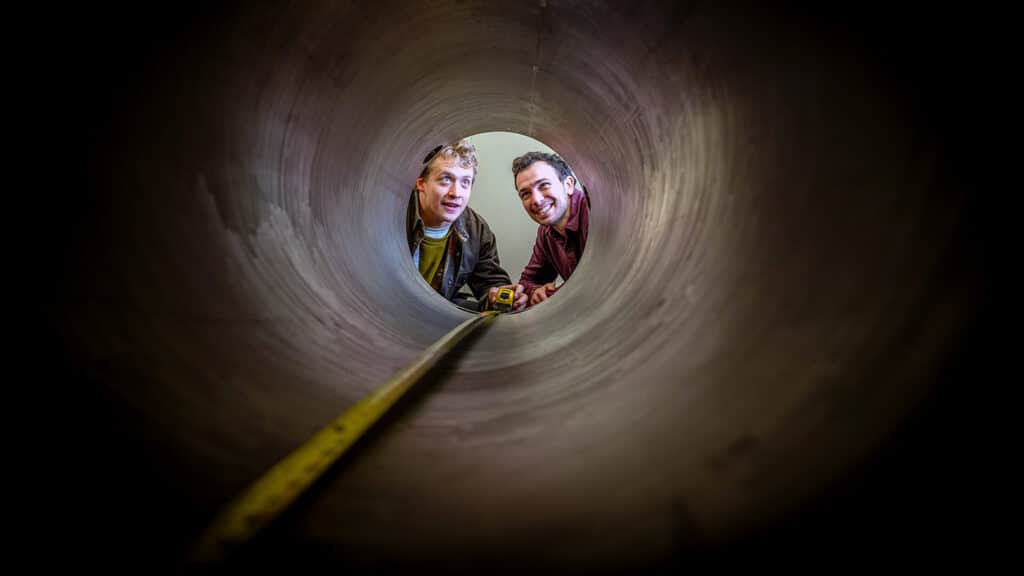 Physics graduate students Cole Teander and Clark Hickman peer from one end of the roundhouse to the other. The roundhouse is a large steel cylindrical structure.