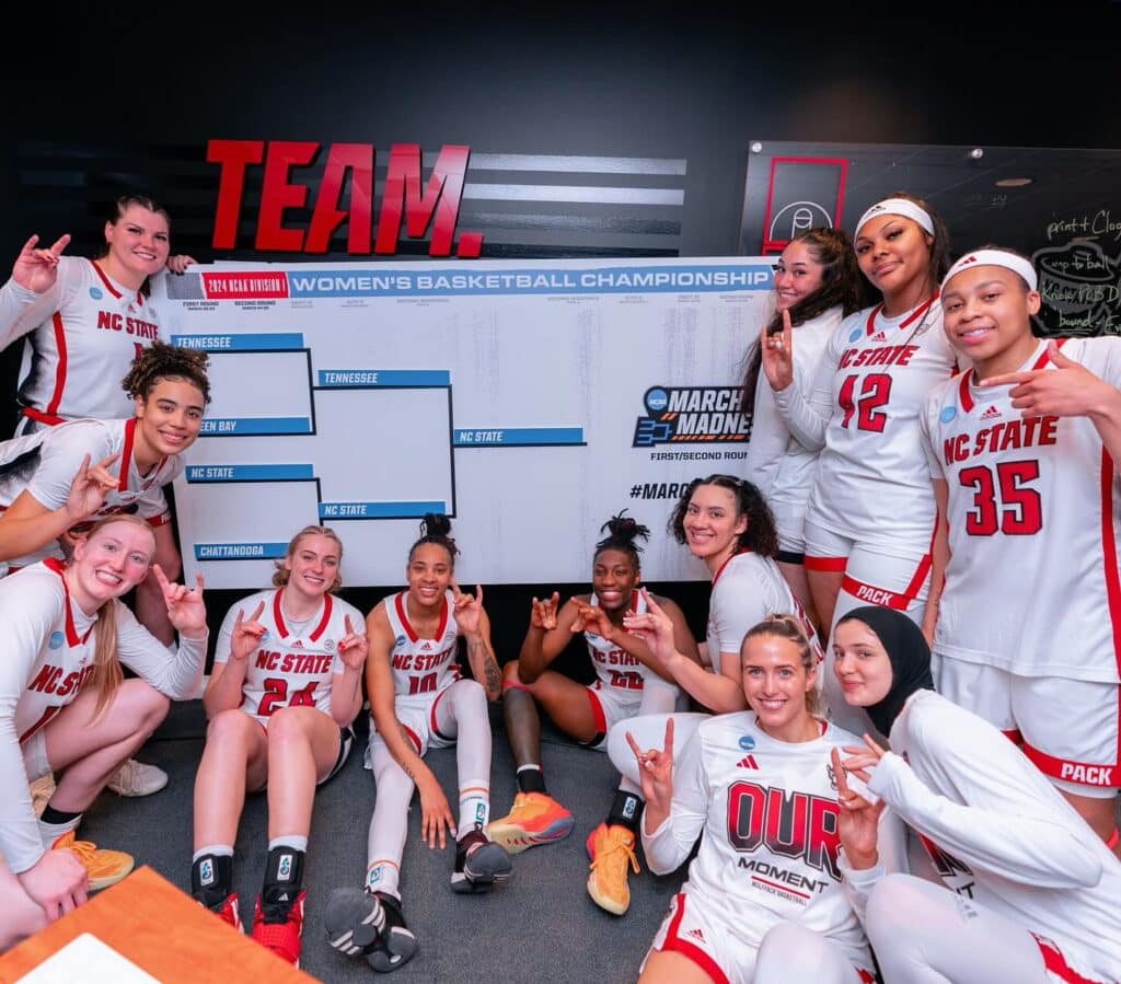 Members of the women's basketball team celebrate in front of a bracket board showing them advancing to the Sweet 16. 