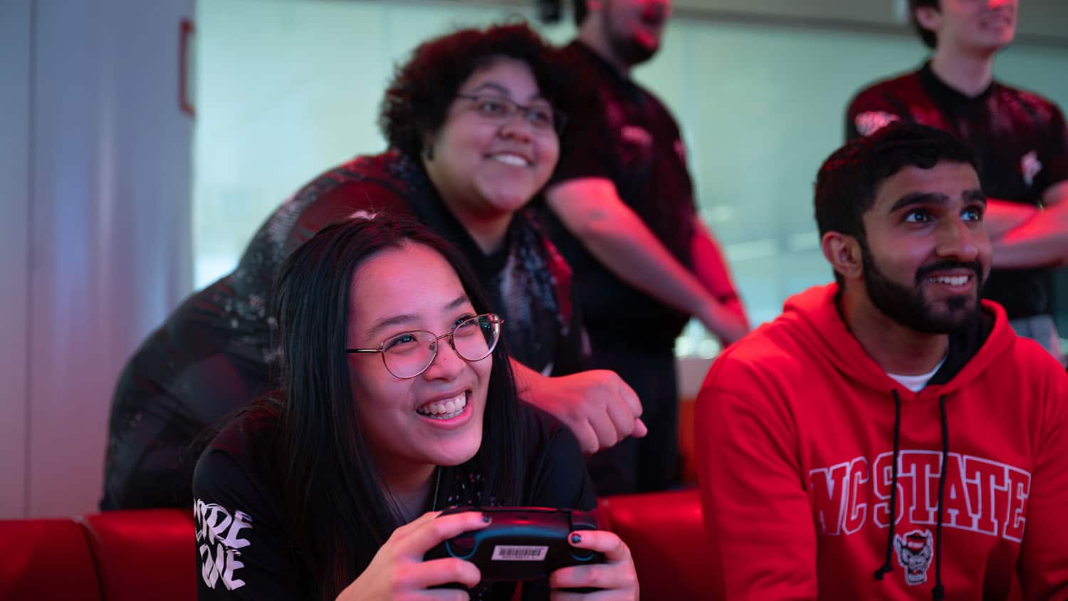 A shot of three students gaming, smiling and celebrating together.