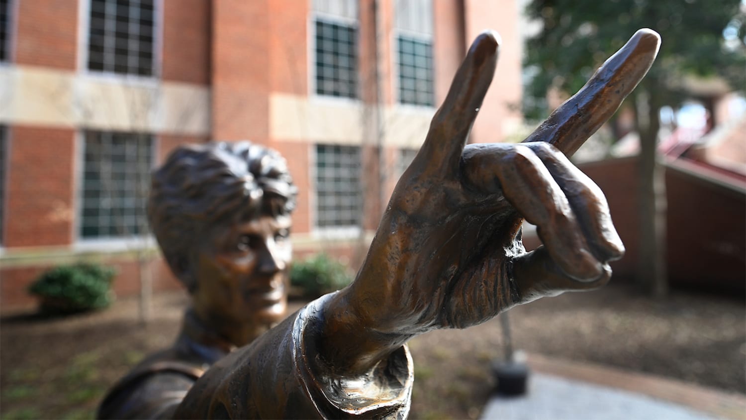 A statue of Kay Yow making wolfie sign with her fingers outside of Reynolds Coliseum