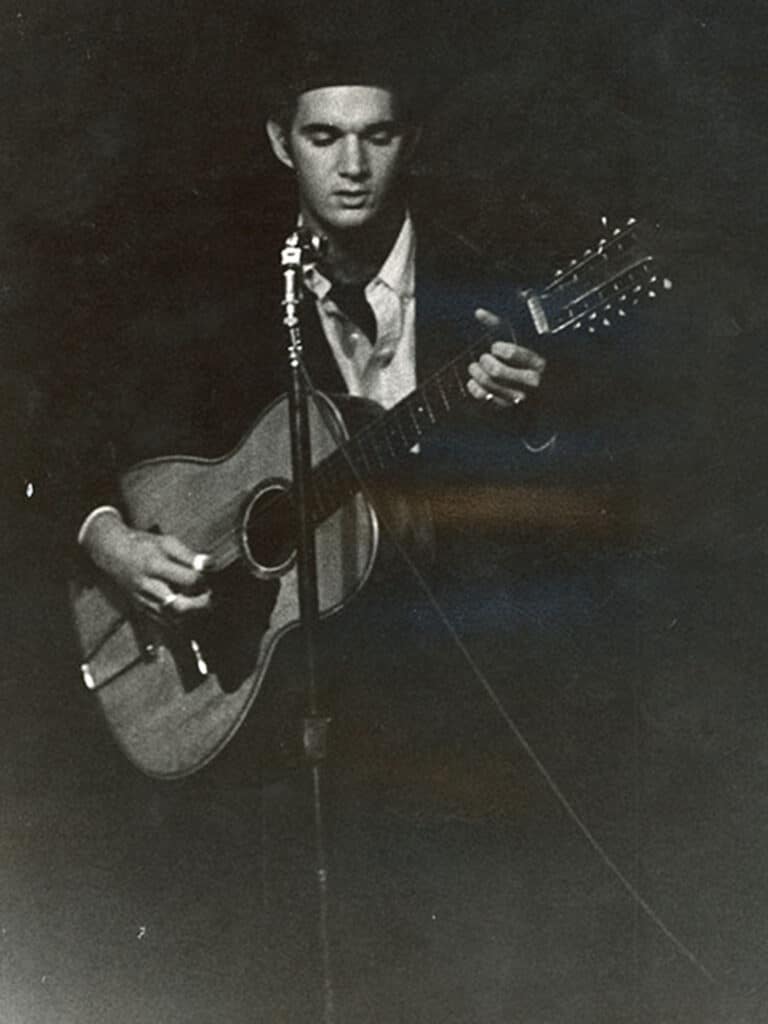 A black-and-white photo shows artist Larry Bell strumming an acoustic guitar in an L.A. nightclub.