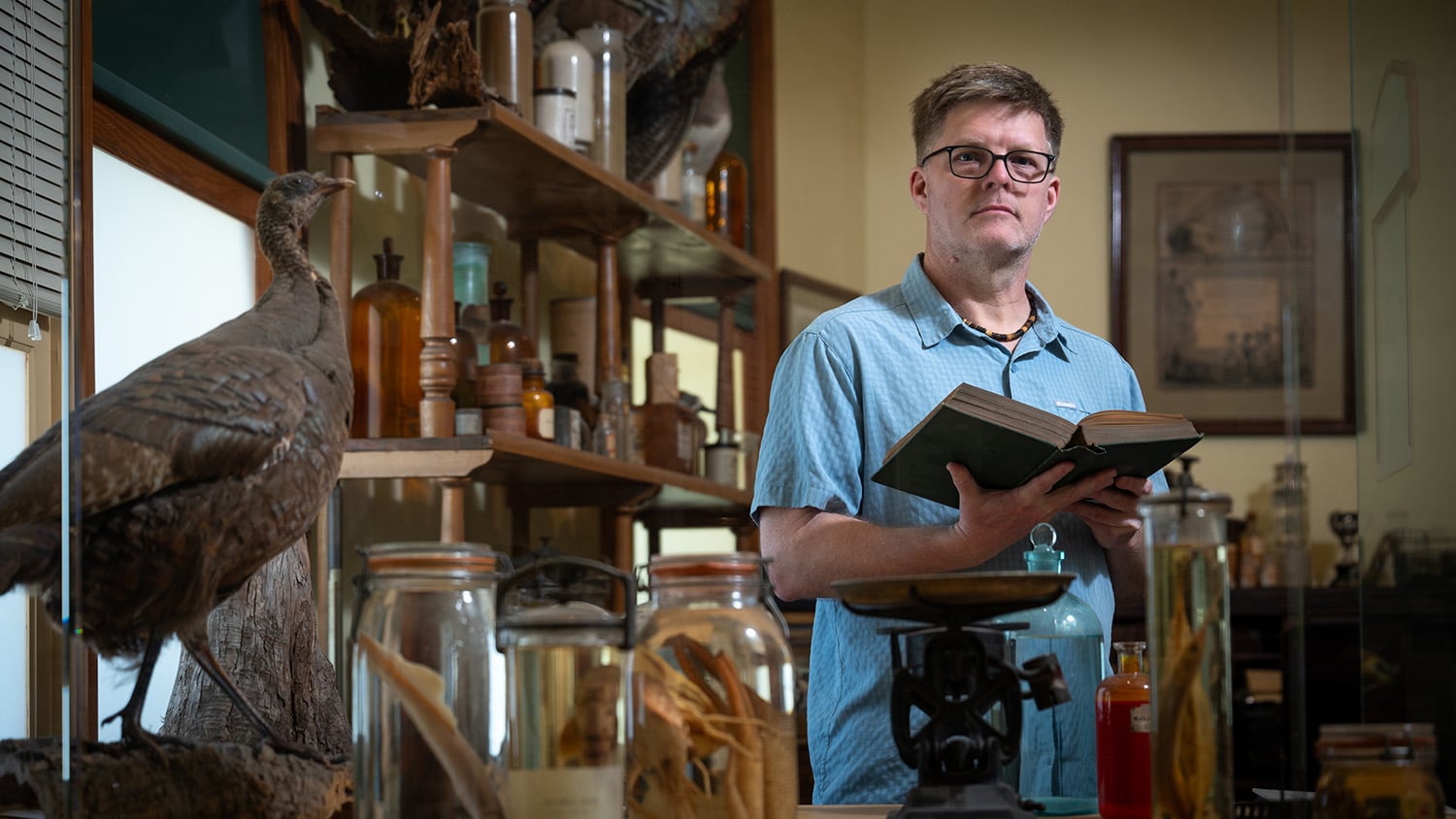 Historian of science Paul Brinkman holds a book in a glass-walled exhibit at the North Carolina Museum of Natural Sciences