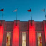 The exterior of Reynolds Coliseum, lit red at night.