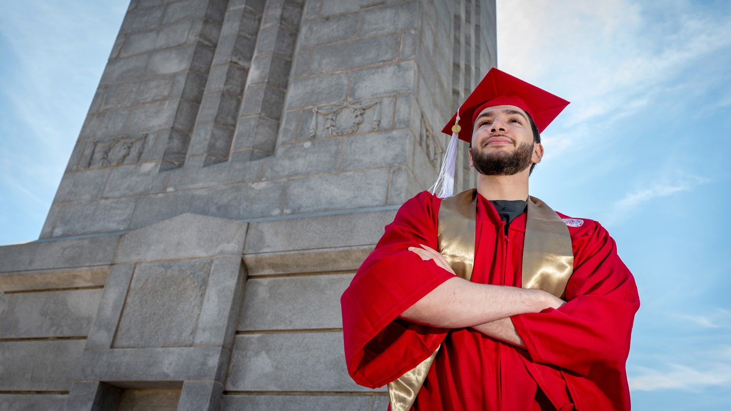 Abdullah Zaben stands in front of the Memorial Belltower wearing his cap and gown.