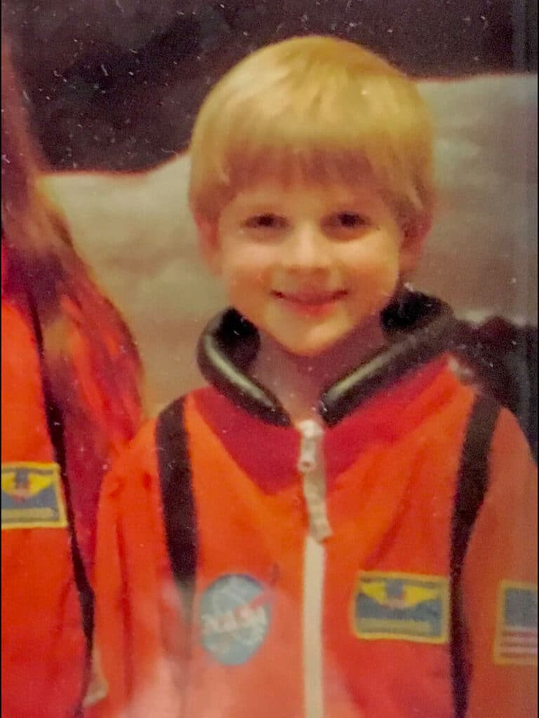 A young child smiles while wearing an orange astronaut uniform.