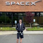 A student smiles in sunglasses in front of a brick building with the SpaceX logo.