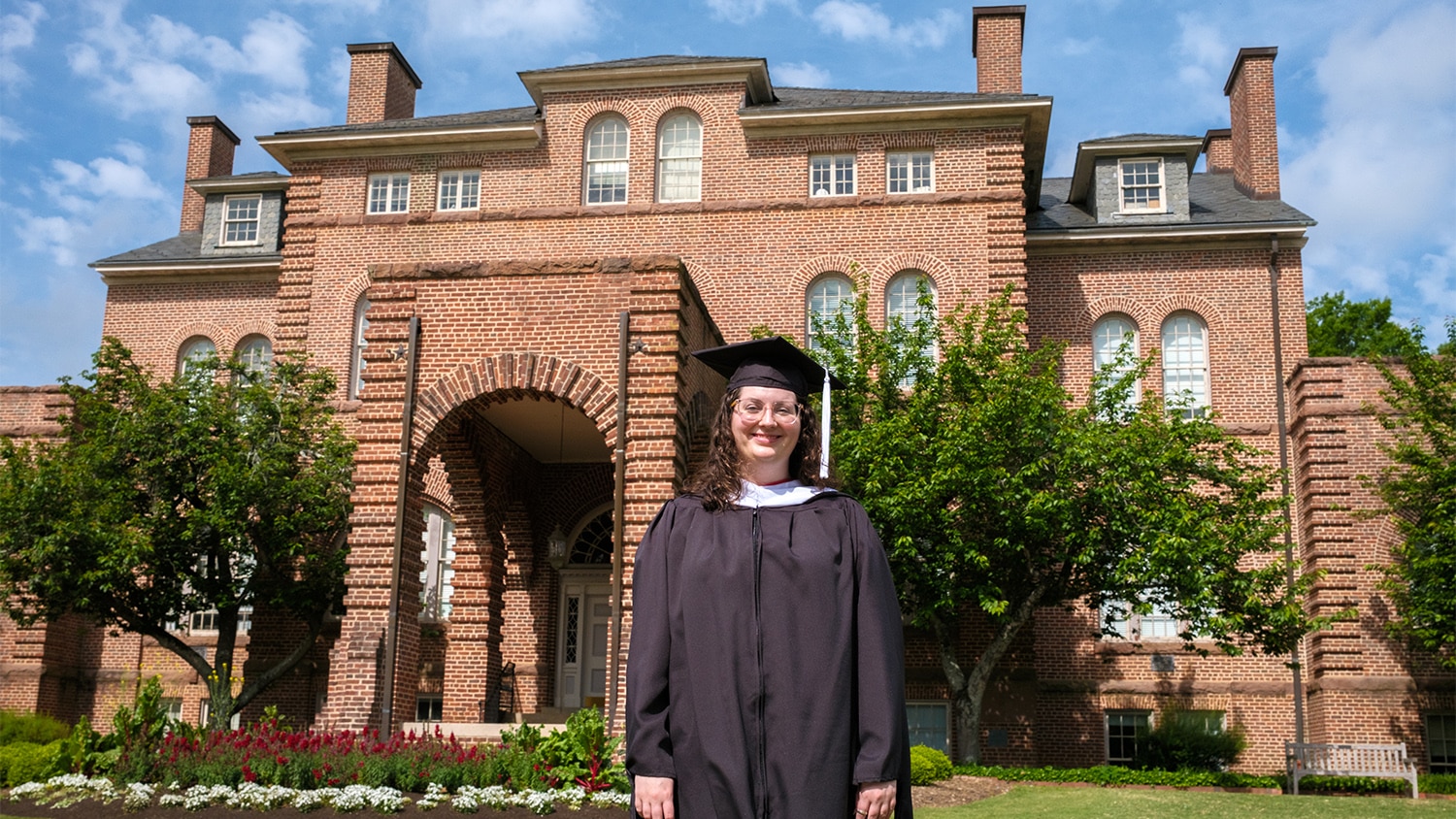Maggie Thompson in her graduation cap and gown, standing in front of Holladay Hall