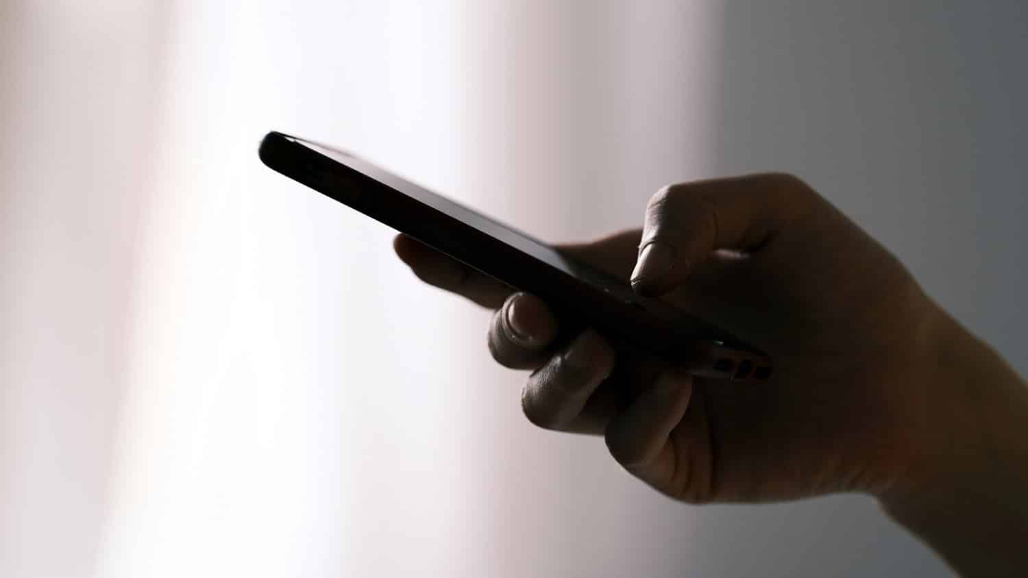 image shows a hand holding a smartphone in silhouette