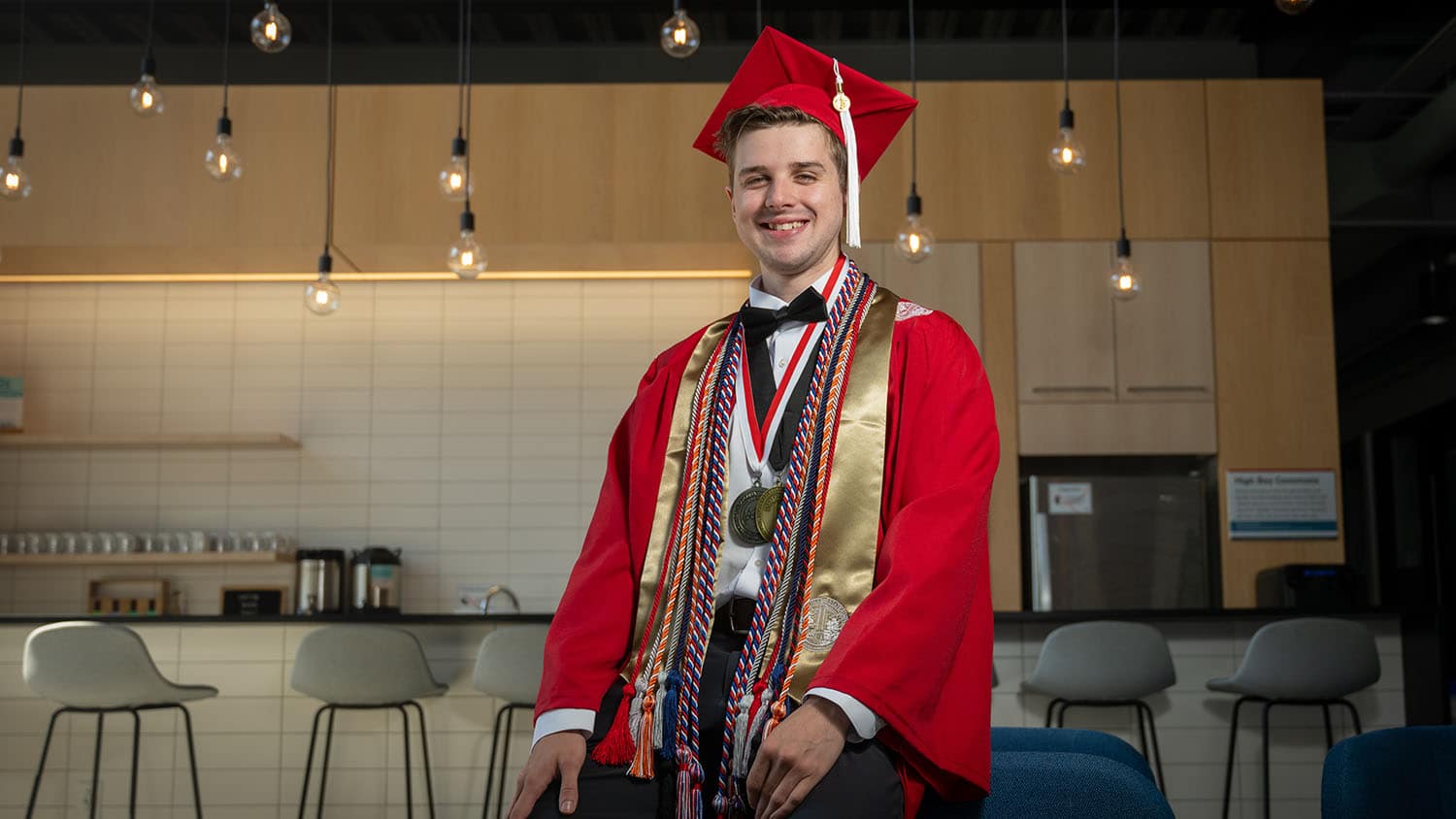 2024 NC State graduate Shaun Deardorff poses in the Raleigh Founded location on Centennial Campus, with lightbulbs shining in the background.
