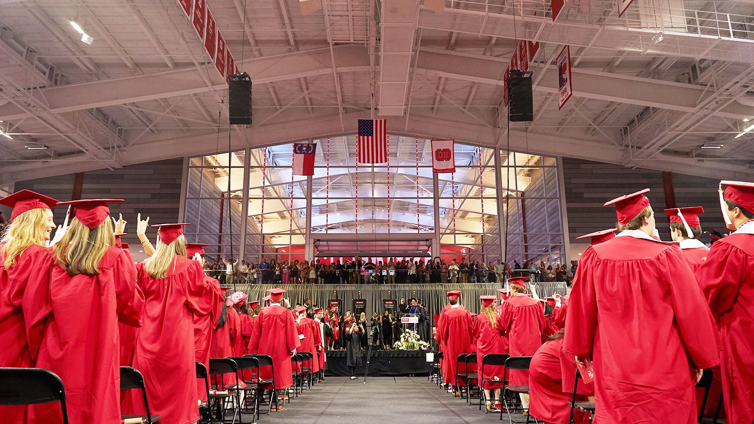 Students wearing red caps and gowns stand during the Poole College of Management's graduation ceremony in Reynolds Coloseum.