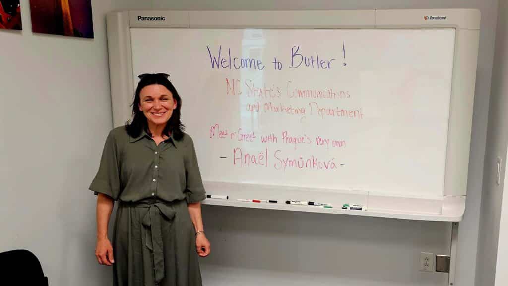 Symůnková standing next to a white board in a conference room that reads "Welcome to Butler! NC State Communications and Marketing Department meet n' greet with Prague's very own Anaël Symůnková."