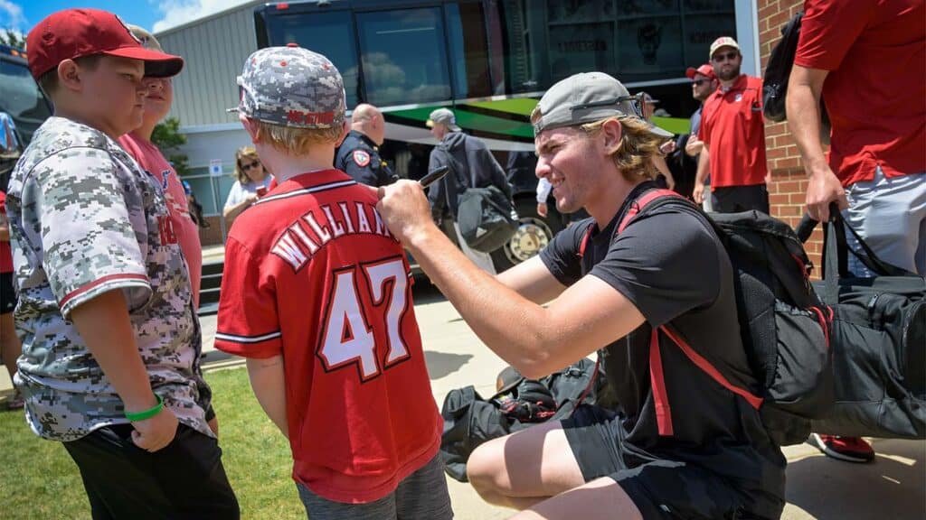 A baseball player signs the jersey of a young fan