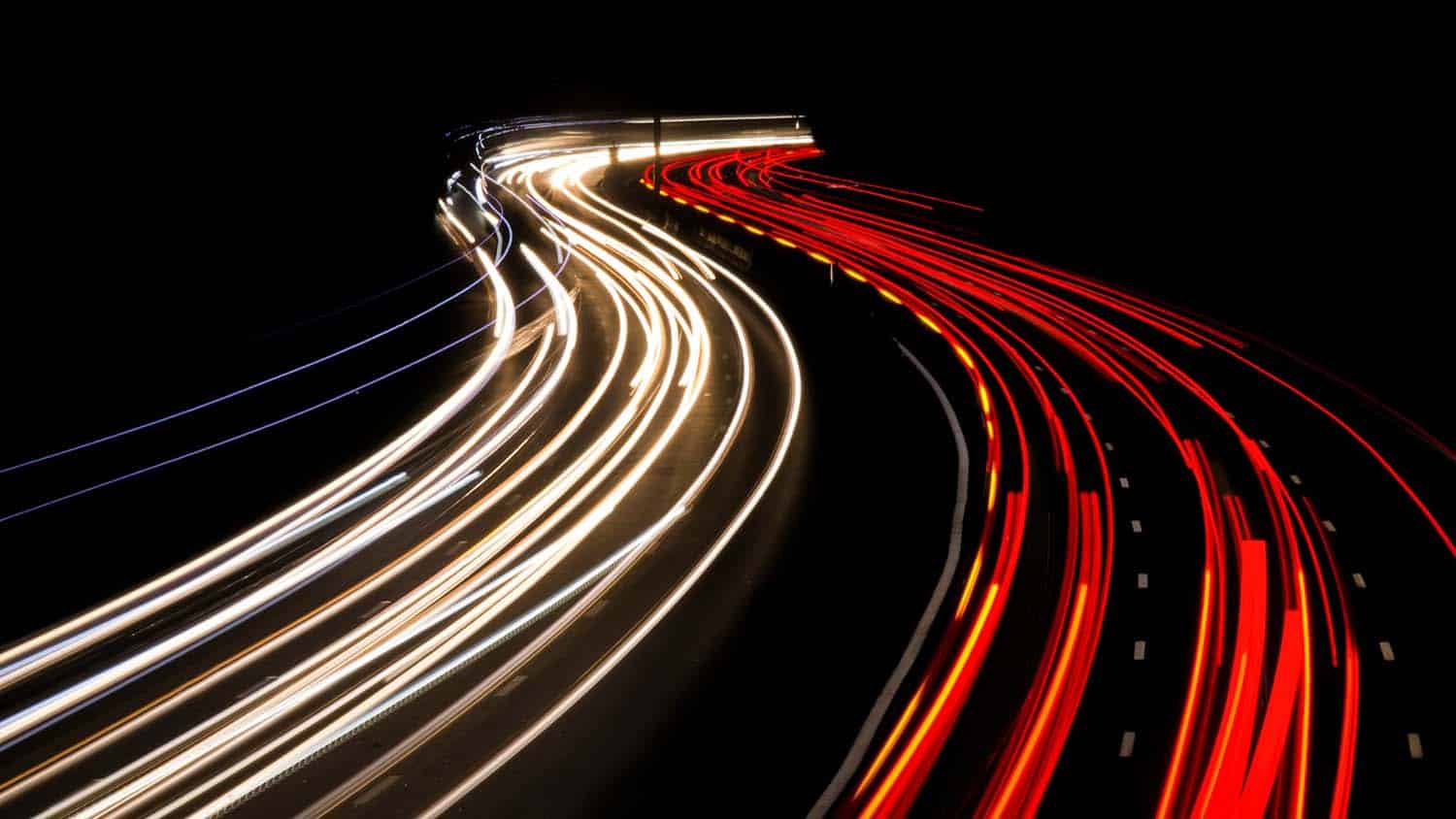 time-lapse photograph shows blurred images of car lights moving in two different directions