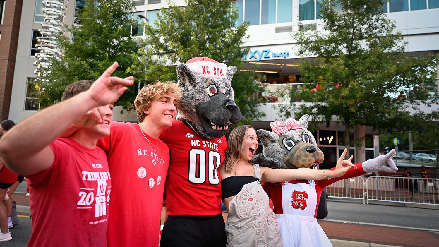 Three students hold up the wolfie hand gesture while posing for a photo with Mr. and Ms. Wuf at Packapalooza.