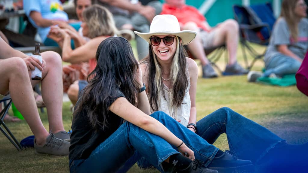 Two women sit on the lawn and chat during a concert.