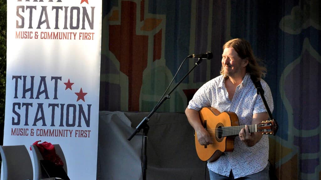 Greg Humphreys smiles and plays the guitar on stage. 