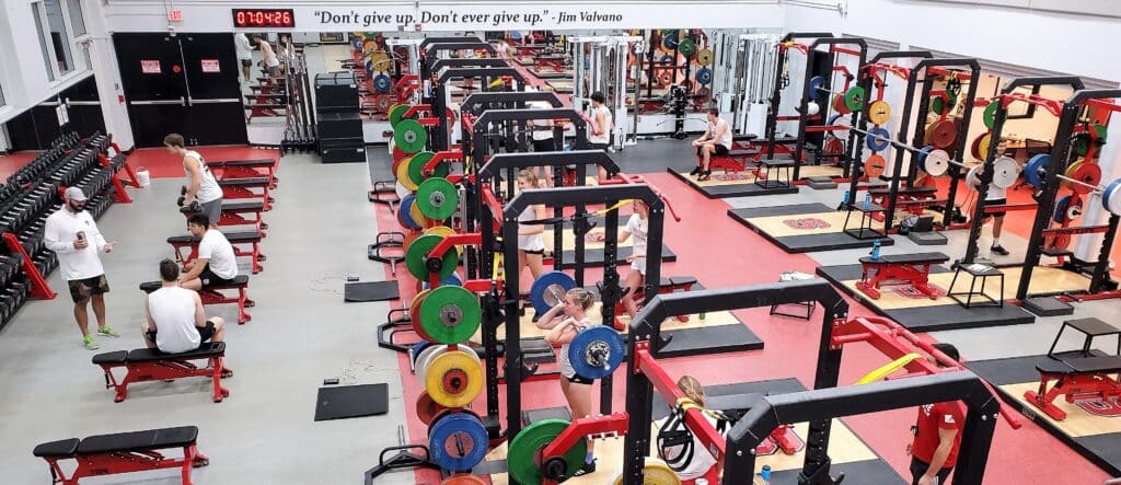 Athletes lift weights and meet with a coach in the weight room