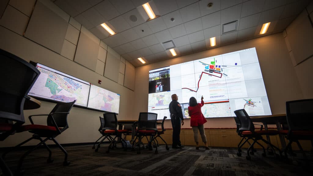 Two NC State employees stand inside the university's Resiliency Operations Center monitoring the screens.