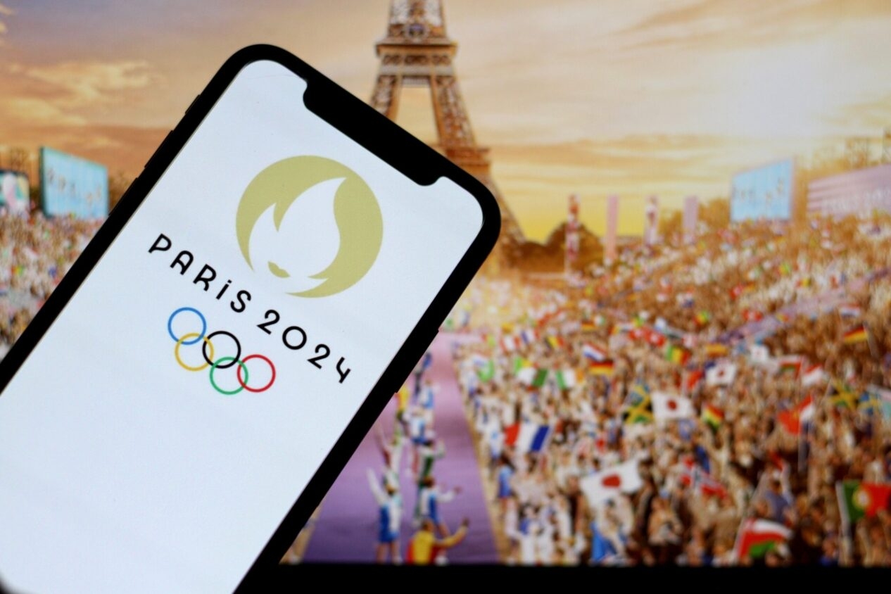 smartphone is held in front of the eiffel tower. the smartphone screen shows the olympics logo