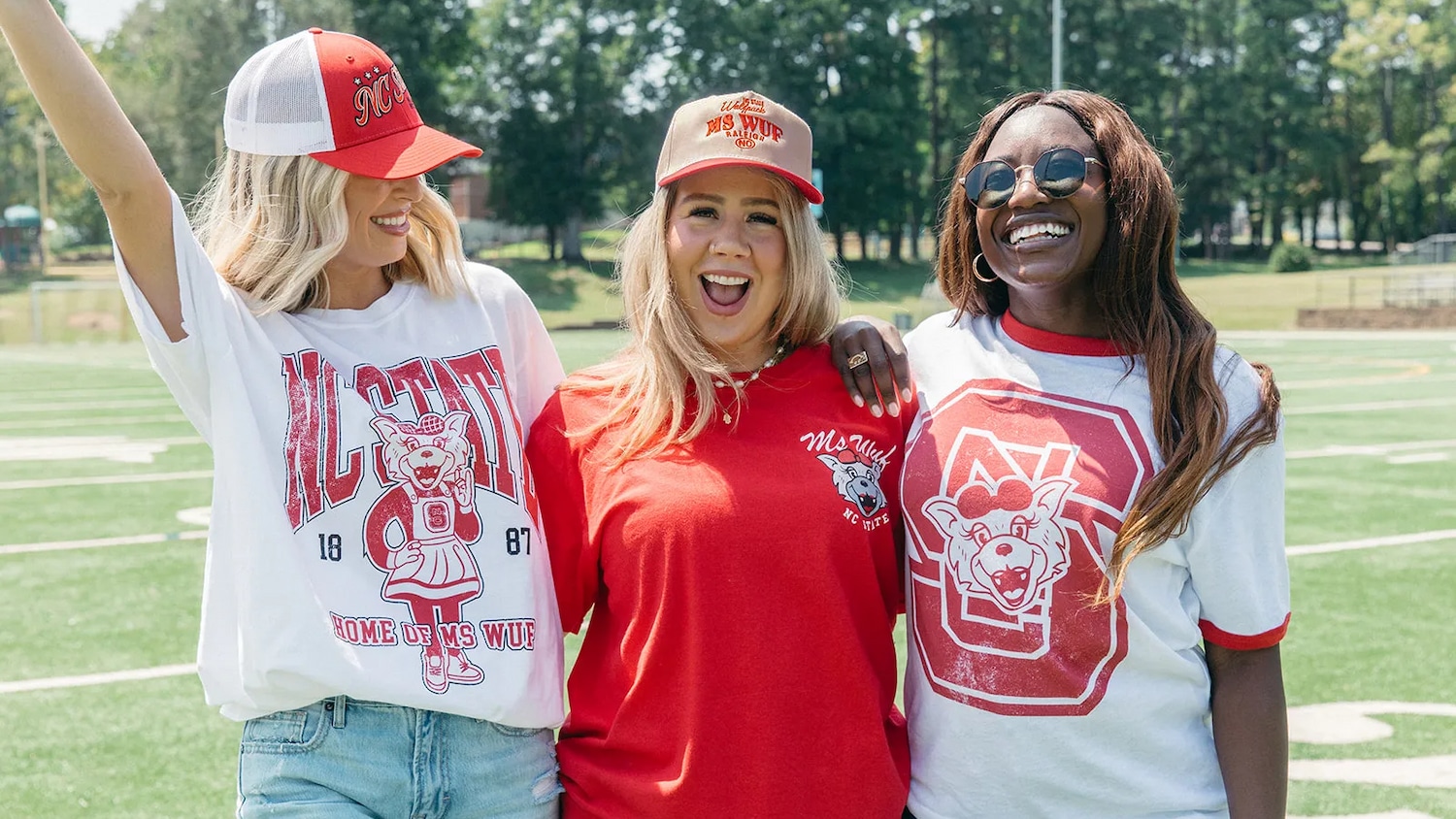 Three smiling women stand together in new Ms. Wuf merchandise.