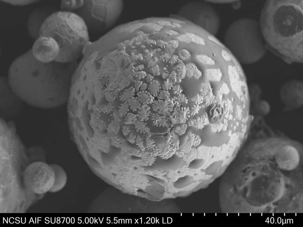 A black-and-white microscopic image of alloy appearing as a spotted sphere with dense dendrites that creates a funky splotch-like effect.