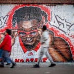 Students walk through the Free Expression Tunnel as a mural of NC State basketball star DJ Burn looks on.